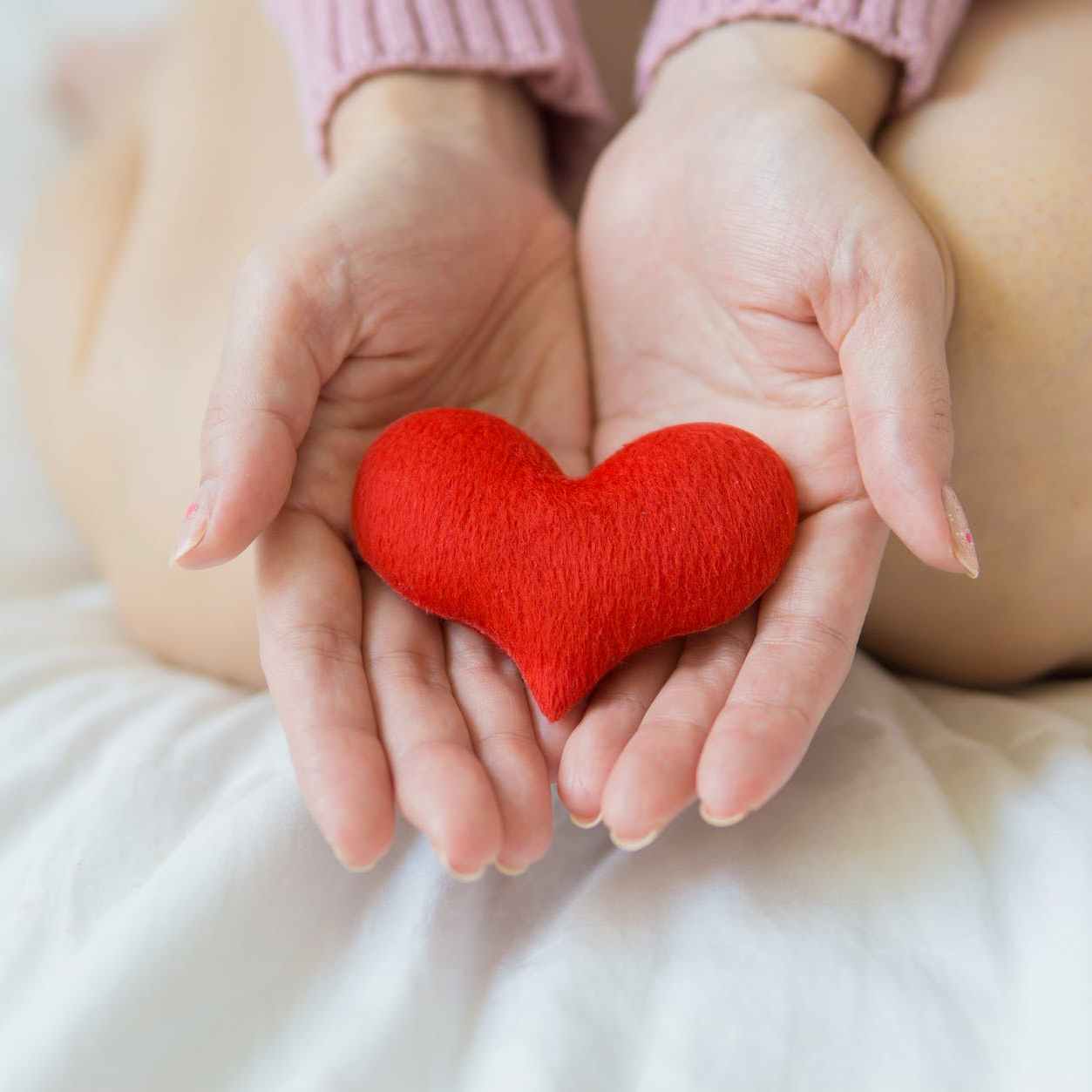 cropped woman sitting on a white blanket with a plush heart on her palms