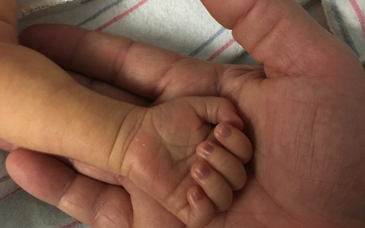 an infant hand laying in an adult hand, palms facing up
