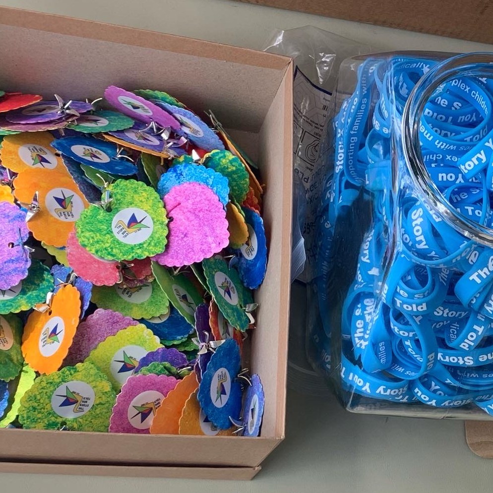 Heart tokens which are made out of paper andsponge painted different colors. There is a sticker of the The Story You Told logo on the front and a small crane charm is tied to the top